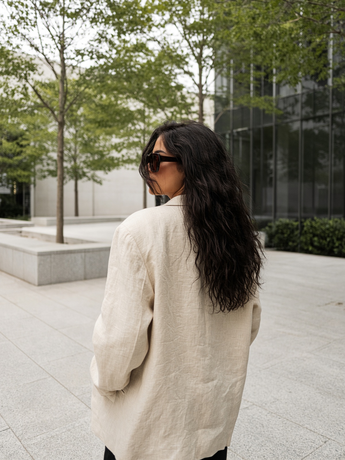 Mulher de costas com óculos de sol oversized em uma praça contemporânea.
